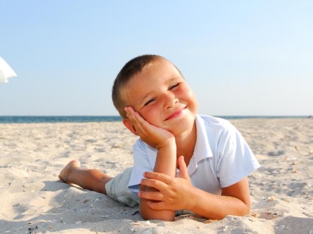 Bambino sorridente sulla spiaggia con ombrellone bianco.