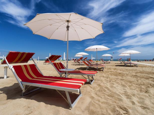 Spiaggia con lettini e ombrelloni bianchi sotto un cielo blu.