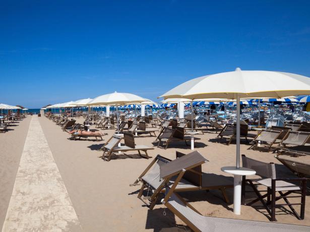 Spiaggia con ombrelloni e lettini, cielo sereno.