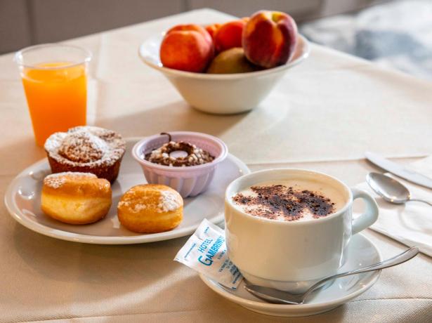 Colazione con dolci, cappuccino, succo d'arancia e frutta fresca.
