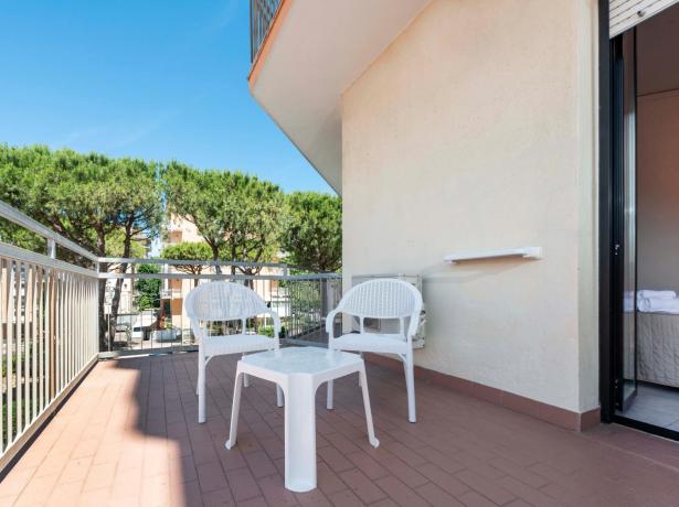 Terrazza con sedie bianche e tavolo, vista alberi.