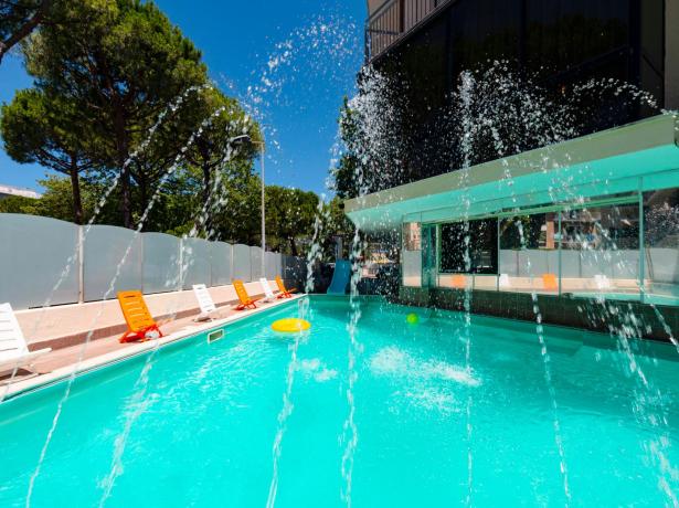 Piscina all'aperto con sedie a sdraio colorate e fontane d'acqua.