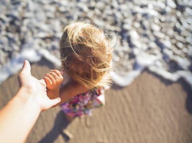 Bambina sulla spiaggia, mano nella mano, onde che si infrangono.