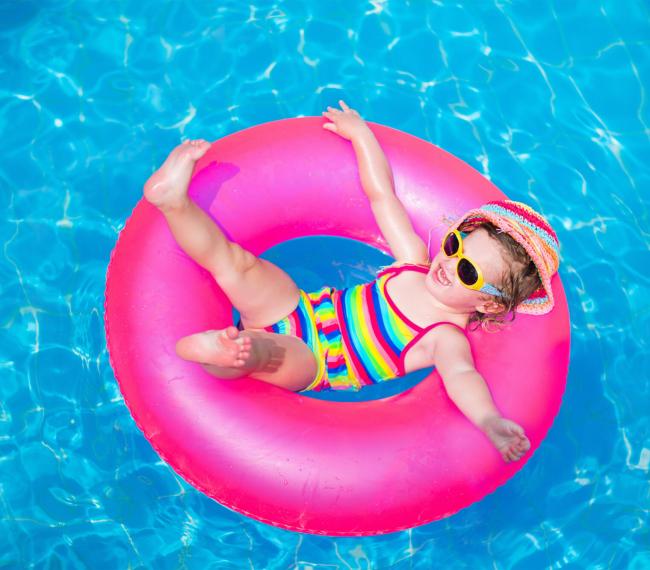 Bambina felice su un salvagente rosa in piscina.