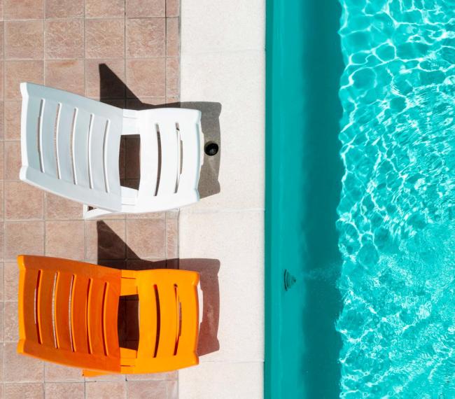 Due sedie colorate accanto a una piscina luminosa.