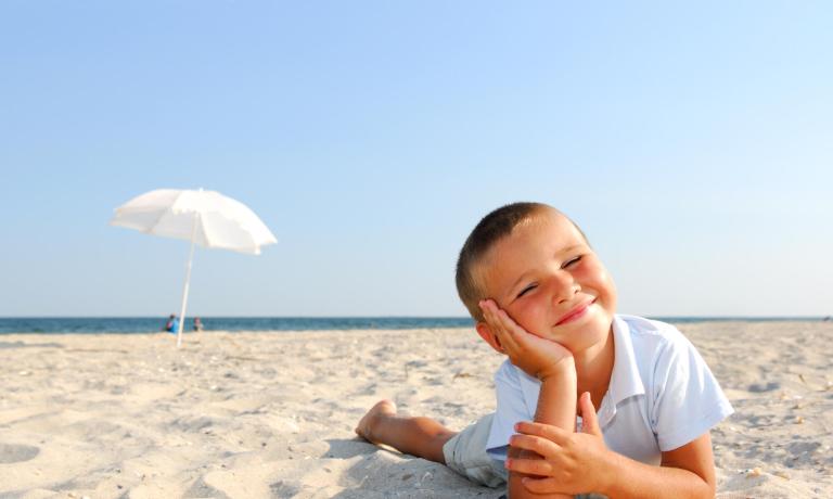 Bambino sorridente sulla spiaggia con ombrellone bianco.