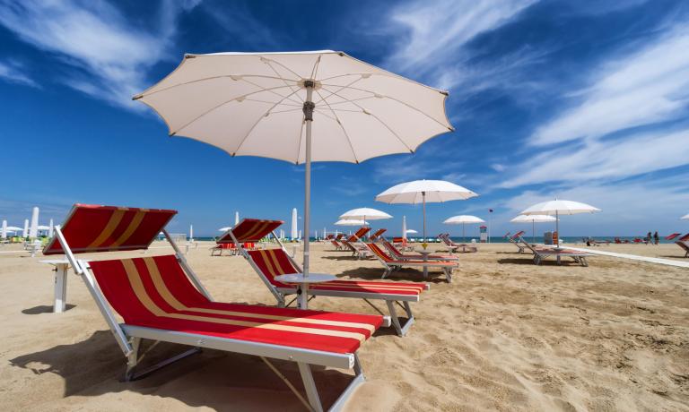 Spiaggia con lettini e ombrelloni bianchi sotto un cielo blu.