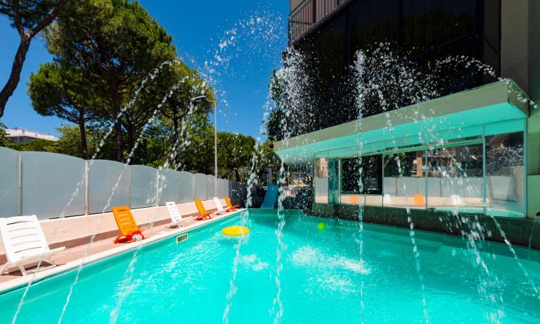 Piscina all'aperto con sedie a sdraio colorate e fontane d'acqua.
