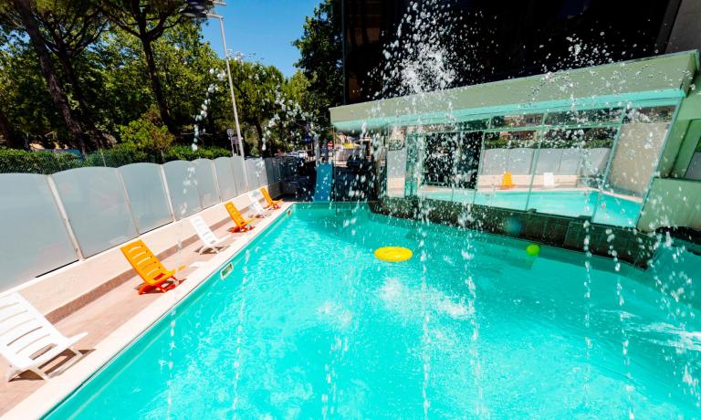 Piscina all'aperto con sedie a sdraio e giochi d'acqua.