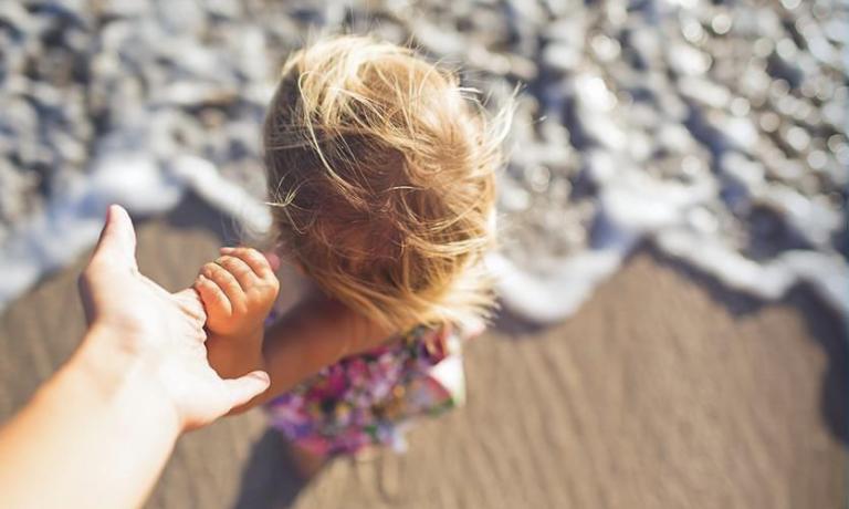 Bambina sulla spiaggia, mano nella mano, onde che si infrangono.